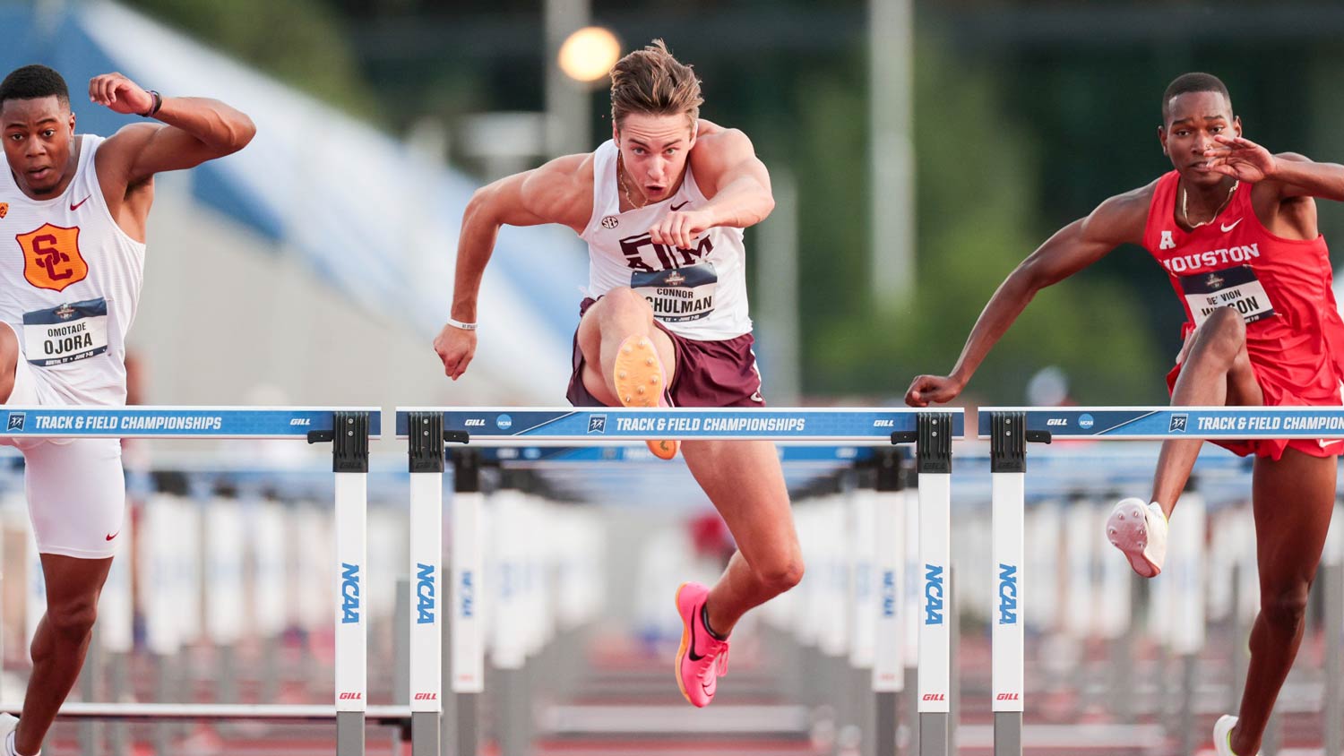 A Texas A&M track athlete leaps over a hurdle during a race