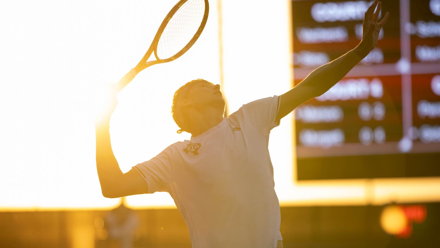 A tennis player serves the ball with a sunset in the background