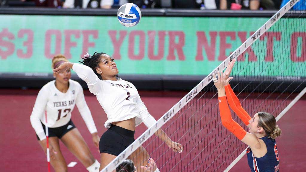 A Texas A&M volleyball player spikes the ball over the net